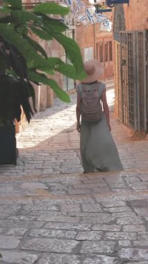 Dikey çekim. Açık havada yürüyorum. Neşeli gülümseyen stil sahibi kadın turist. Eski şehrin sokaklarında yürüyen bir gezgin. Seyahat ve tatil.