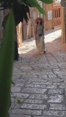 Dikey çekim. Açık havada yürüyorum. Neşeli gülümseyen stil sahibi kadın turist. Eski şehrin sokaklarında yürüyen bir gezgin. Seyahat ve tatil.