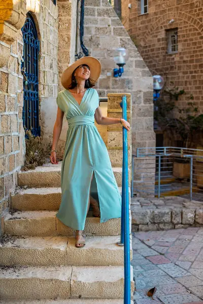 Neşeli gülümseyen stil sahibi bayan turist. Eski Jaffa şehrinde güzel caddelerde yürüyen elbiseli genç bir kadın. İsrail. Seyahat ve macera.