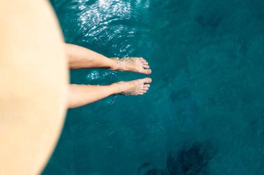 Kız iskelede oturuyor ve ayaklarını denizin mavi ve şeffaf sularına koyuyor. Yaz havası. Güzel ince ve bronzlaşmış bacakları olan bir kadın. Suda dinlenen bir kadın. Ayaklarını suya çarpan bir kadın..