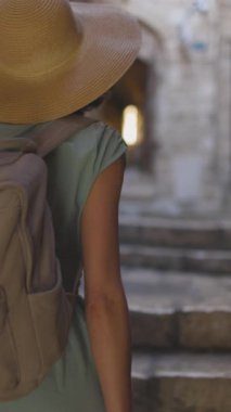 Dikey çekim. Elbiseli bir kız eski şehrin dar sokaklarında yürüyor. Eski Jaffa şehrinde güzel caddelerde yürüyen elbiseli genç bir kadın. İsrail. seyahat ve macera.