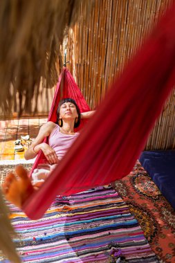 Tatilde hamakta dinlenen sakin bir genç kadın. Kız rahat bir şekilde dışarıda hamakta sallanıyor, stressiz bir hayat sürüyor. Yaz havası.