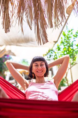 Tatilde hamakta dinlenen sakin bir genç kadın. Kız rahat bir şekilde dışarıda hamakta sallanıyor, stressiz bir hayat sürüyor. Yaz havası.