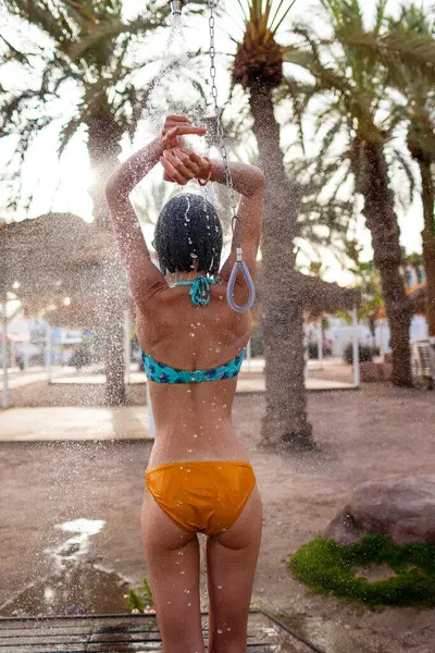 Yaz havası. Güneşli bir günde, plajdaki lüks bir otelde mayo giymiş esmer, beyaz bir kadın ferahlatıcı bir tropikal duş alıyor. Mayolu kız..