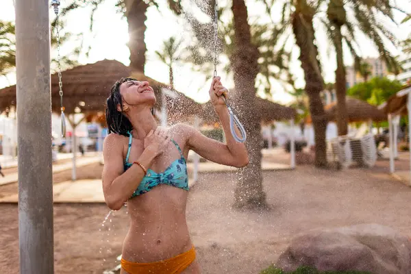 Mayo giymiş ince bir kadın gün batımında duş alıyor. Kız sahilde duş alıyor, deniz kenarında. Yaz havası. Mayolu kız..