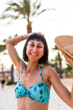 Şapkalı güzel bir genç kadının portresi. Yaz havası. Kameraya gülümseyen ve sahilde tatilin tadını çıkaran mutlu kadın. Mayolu kız..