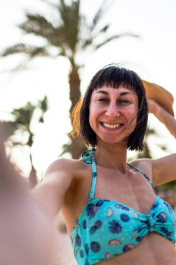 Tropikal plajda bikinili ve şapkalı güzel bir kadın. Yaz havası. Mutlu gezgin, tropik sahilde tatilin tadını çıkarıyor..