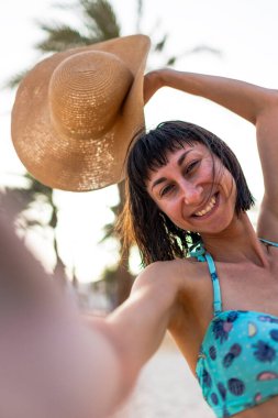 Tropikal plajda bikinili ve şapkalı güzel bir kadın. Yaz havası. Mutlu gezgin, tropik sahilde tatilin tadını çıkarıyor..