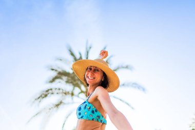 Şapkalı güzel bir genç kadının portresi. Yaz havası. Kameraya gülümseyen ve sahilde tatilin tadını çıkaran mutlu kadın. Mayolu kız..