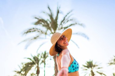 Tropikal plajda bikinili ve şapkalı güzel bir kadın. Yaz havası. Mutlu gezgin, tropik sahilde tatilin tadını çıkarıyor..