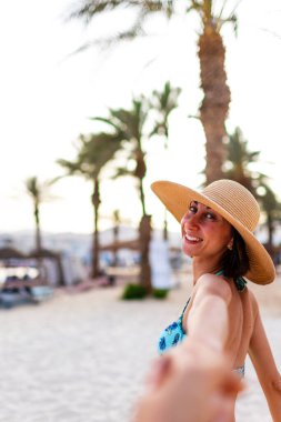 Tropik cennet sahilinde bikinili güzel bir kadın. Yaz havası. Mutlu bronzlaşmış kadın portresi gülümseyen ve kameraya elini uzatarak beni takip etmeni istiyor. Mayolu kız..