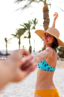Tropik cennet sahilinde bikinili güzel bir kadın. Yaz havası. Mutlu bronzlaşmış kadın portresi gülümseyen ve kameraya elini uzatarak beni takip etmeni istiyor. Mayolu kız..