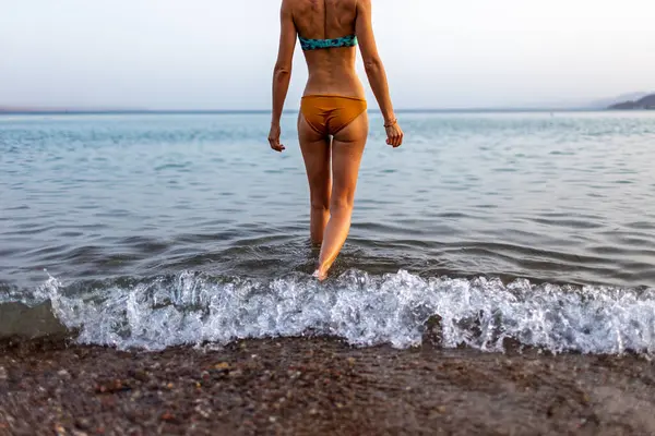 Sahildeki kız. Bacaklar yakın plan. Kaygısız genç kız Kızıl Deniz 'in arka planında yürüyor. Seyahat ve tatil.