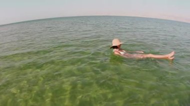 Ölü Deniz 'de yüzmekten zevk alan bir kız. Talassotherapy gören bir kadın, Ölü' nün açık yeşil sularında sakin bir şekilde yüzüyor.