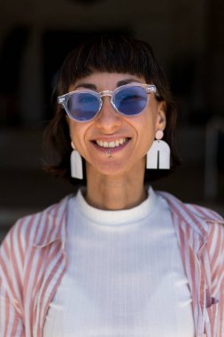 Mutlu kadın portresi ve alt dudağında piercing, kendine güven veya şehirde neşeli bir tutum. Kadın, esmer, gülümseyen kamera, mücevher ve şık moda şehirlerde.