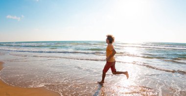 Adam kumsalda koşuyor. Güneşli bir yaz gününde fitness antrenmanı. Sahilde koşmak. spor ve sağlık.