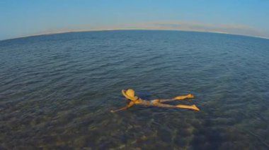 Güzel ölü deniz suyunda yüzen kadın, yaz tatili konsepti. Kristal gibi berrak yüzeyde dinlenen genç bir kadın görüntüsü