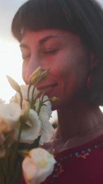 Dikey çekim. Gün ışığında bir buket taze bahar çiçeğiyle gülümseyen kadın yüzünü kapat. Çiçekten zevk alan mutlu kızın yüzü