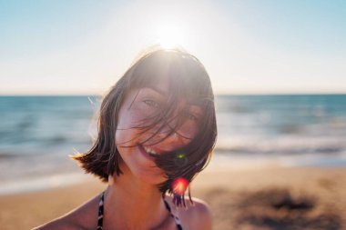 Kumsalda güzel bir esmerin portresi. Genç mutlu kız gülümsüyor. Saç yüzünü kapatır. Rüzgar saçlarınla oynuyor. Yüz kılları. Yaz tropik havası