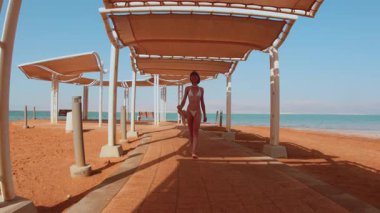 Bikinili bir kadın deniz kenarında yürümekten hoşlanıyor, tatildeki bir kız. Sur boyunca yürüyen güzel bir kadın. Yaz havası.