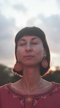 Dikey çekim. Gün batımında gözleri kapalı güzel bir kadının portresi. Kız gün batımının tadını çıkarıyor. Romantik ruh hali