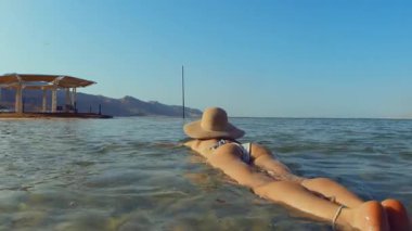 Sıska kız Ölü Deniz 'in sularında rahatça yüzüyor. Şapkalı kız tatilin tadını çıkarıyor. Yaz havası. Ölü Deniz. İsrail.
