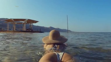 Denizde yüzen bir kadın. Şapkalı ve mayo giymiş bir kız rahatlamış. Şapkalı kız tatilinin tadını çıkarıyor. Yaz havası. Öldü.