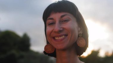 Kameraya bakan gülümseyen genç bir kadının portresi. Mutlu hissediyorum. Dışarıda, gün ışığında. Romantik bir ruh hali. Yavaş çekim