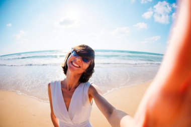 Sevimli, şaşkın, güzel bir kızın sahilde yürürken ve kameraya selfie çekerken çekilmiş fotoğrafı. Kız selfie çekiyor..