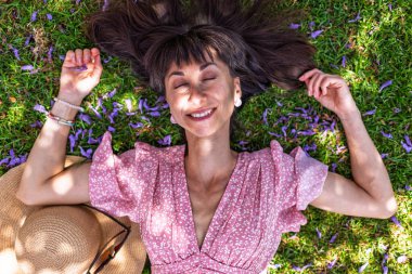 Yeşil çimlerin üzerinde yatan genç bir kadın. Yaz havası. Kız dışarıda vakit geçiriyor. Doğanın tadını çıkar. Üst Manzara. Sağlıklı gülümseyen kız baharda çimlerde.