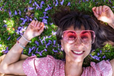 Yaz havası. Yeşil çimlerin ve çiçeklerin üzerinde yatan genç bir kadın. Yaz havası. Kız dışarıda vakit geçiriyor. Doğanın ve tatilin tadını çıkar. Mutlu kadın..