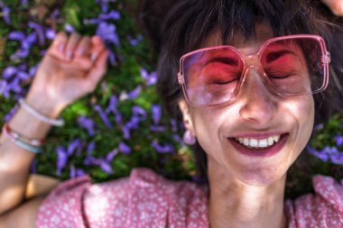 Yaz havası. Yeşil çimlerin ve çiçeklerin üzerinde yatan genç bir kadın. Yaz havası. Kız dışarıda vakit geçiriyor. Doğanın ve tatilin tadını çıkar. Mutlu kadın..