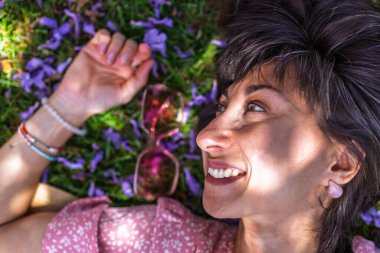 Yaz havası. Yeşil çimlerin ve çiçeklerin üzerinde yatan genç bir kadın. Yaz havası. Kız dışarıda vakit geçiriyor. Doğanın ve tatilin tadını çıkar. Mutlu kadın..