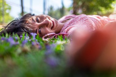 Yeşil çimlerin üzerinde yatan genç bir kadın. Yaz havası. Kız dışarıda vakit geçiriyor. Doğanın tadını çıkar. Sağlıklı gülümseyen kız baharda çimlerde.