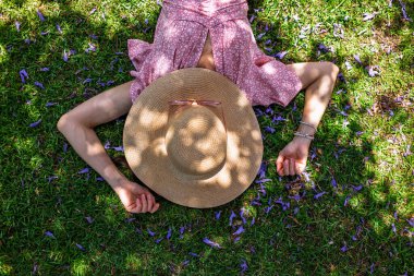 Hasır şapkalı mutlu kız yaz parkında yeşil çimlerin üzerinde uzanmış, manzaralı. Yaz havası. Kız dışarıda vakit geçiriyor. Doğanın tadını çıkar.