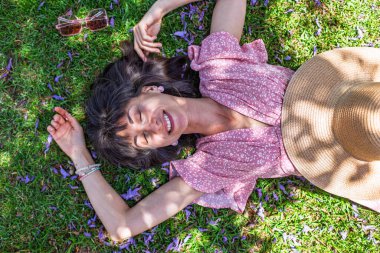 Yeşil çimlerin üzerinde yatan genç bir kadın. Yaz havası. Kız dışarıda vakit geçiriyor. Doğanın tadını çıkar. Üst Manzara. Sağlıklı gülümseyen kız baharda çimlerde.