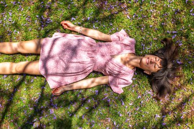 Yaz havası. Yeşil çimlerin ve çiçeklerin üzerinde yatan genç bir kadın. Yaz havası. Kız dışarıda vakit geçiriyor. Doğanın ve tatilin tadını çıkar. Mutlu kadın..