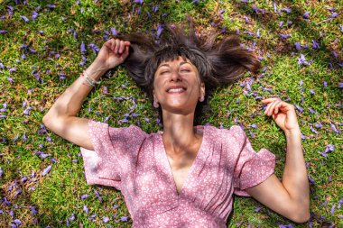 Yaz havası. Yeşil çimlerin ve çiçeklerin üzerinde yatan genç bir kadın. Yaz havası. Kız dışarıda vakit geçiriyor. Doğanın ve tatilin tadını çıkar. Mutlu kadın..