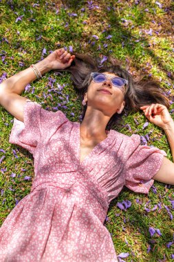 Yaz havası. Yeşil çimlerin ve çiçeklerin üzerinde yatan genç bir kadın. Yaz havası. Kız dışarıda vakit geçiriyor. Doğanın ve tatilin tadını çıkar. Mutlu kadın..