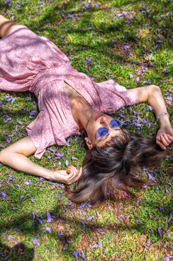 Yaz havası. Yeşil çimlerin ve çiçeklerin üzerinde yatan genç bir kadın. Yaz havası. Kız dışarıda vakit geçiriyor. Doğanın ve tatilin tadını çıkar. Mutlu kadın..