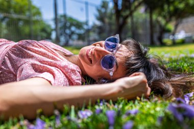 Yeşil çimenlerin ve çiçeklerin üzerinde yatan genç bir kadın. Şapka yüzünü örtüyor. Yaz havası. Kız dışarıda vakit geçiriyor. Doğanın tadını çıkar.