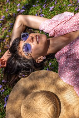 Yaz havası. Yeşil çimlerin ve çiçeklerin üzerinde yatan genç bir kadın. Yaz havası. Kız dışarıda vakit geçiriyor. Doğanın ve tatilin tadını çıkar. Mutlu kadın..