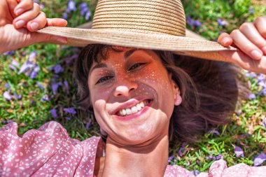 Yeşil çimlerin üzerinde yatan genç bir kadın. Yaz havası. Kız dışarıda vakit geçiriyor. Doğanın tadını çıkar. Üst Manzara. Sağlıklı gülümseyen kız baharda çimlerde.