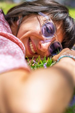 Yeşil çimenlerin ve çiçeklerin üzerinde yatan genç bir kadın. Şapka yüzünü örtüyor. Yaz havası. Kız dışarıda vakit geçiriyor. Doğanın tadını çıkar.