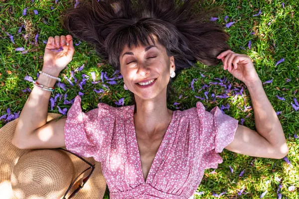 Yeşil çimlerin üzerinde yatan genç bir kadın. Yaz havası. Kız dışarıda vakit geçiriyor. Doğanın tadını çıkar. Üst Manzara. Sağlıklı gülümseyen kız baharda çimlerde.