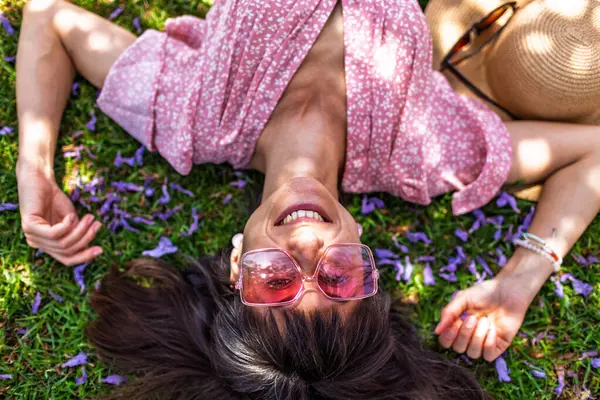 Yeşil çimenlerin ve çiçeklerin üzerinde yatan genç bir kadın. Şapka yüzünü örtüyor. Yaz havası. Kız dışarıda vakit geçiriyor. Doğanın tadını çıkar.