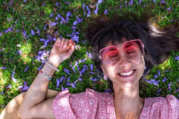 Yeşil çimlerin üzerinde yatan genç bir kadın. Yaz havası. Kız dışarıda vakit geçiriyor. Doğanın tadını çıkar. Üst Manzara. Sağlıklı gülümseyen kız baharda çimlerde.