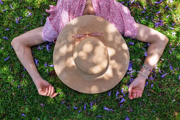 Hasır şapkalı mutlu kız yaz parkında yeşil çimlerin üzerinde uzanmış, manzaralı. Yaz havası. Kız dışarıda vakit geçiriyor. Doğanın tadını çıkar.