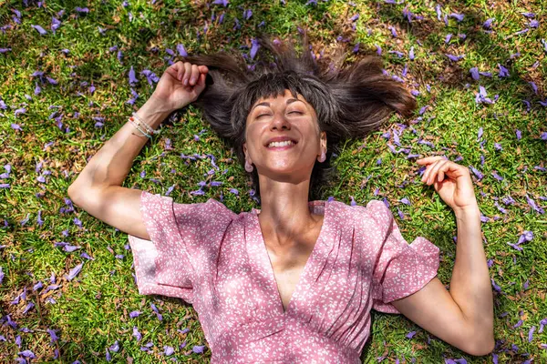 Yaz havası. Yeşil çimlerin ve çiçeklerin üzerinde yatan genç bir kadın. Yaz havası. Kız dışarıda vakit geçiriyor. Doğanın ve tatilin tadını çıkar. Mutlu kadın..