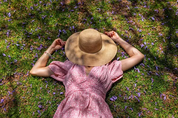 Yeşil çimenlerin ve çiçeklerin üzerinde yatan genç bir kadın. Şapka yüzünü örtüyor. Yaz havası. Kız dışarıda vakit geçiriyor. Doğanın tadını çıkar.